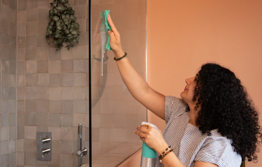 person uses bathroom cleaner on shower glass