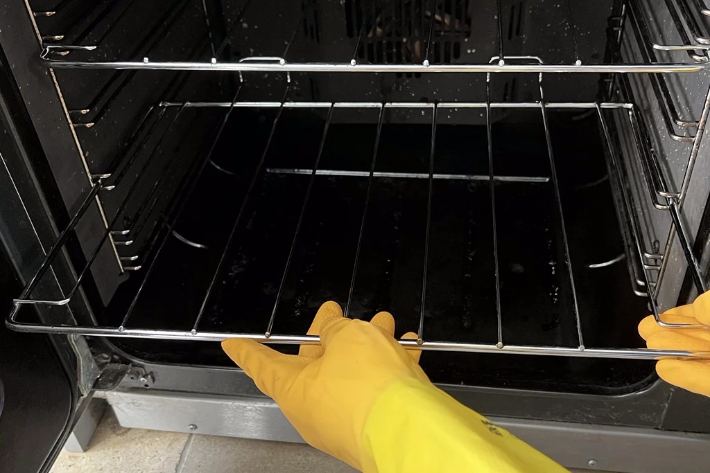 Mains gantées remettant la grille propre à l’intérieur du four.