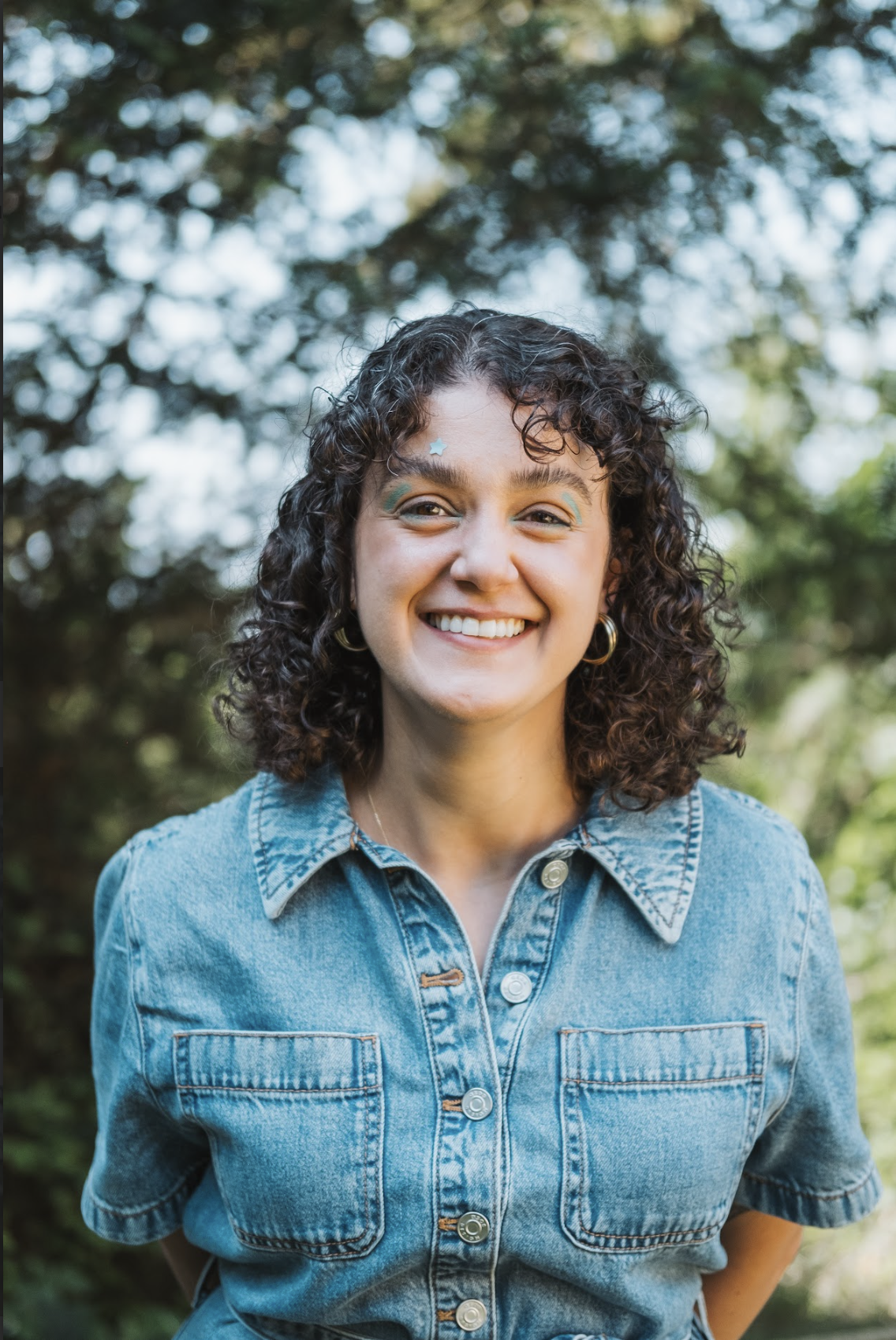 nay gulsan, a woman with dark shoulder length curly hair is smiling against a background of trees