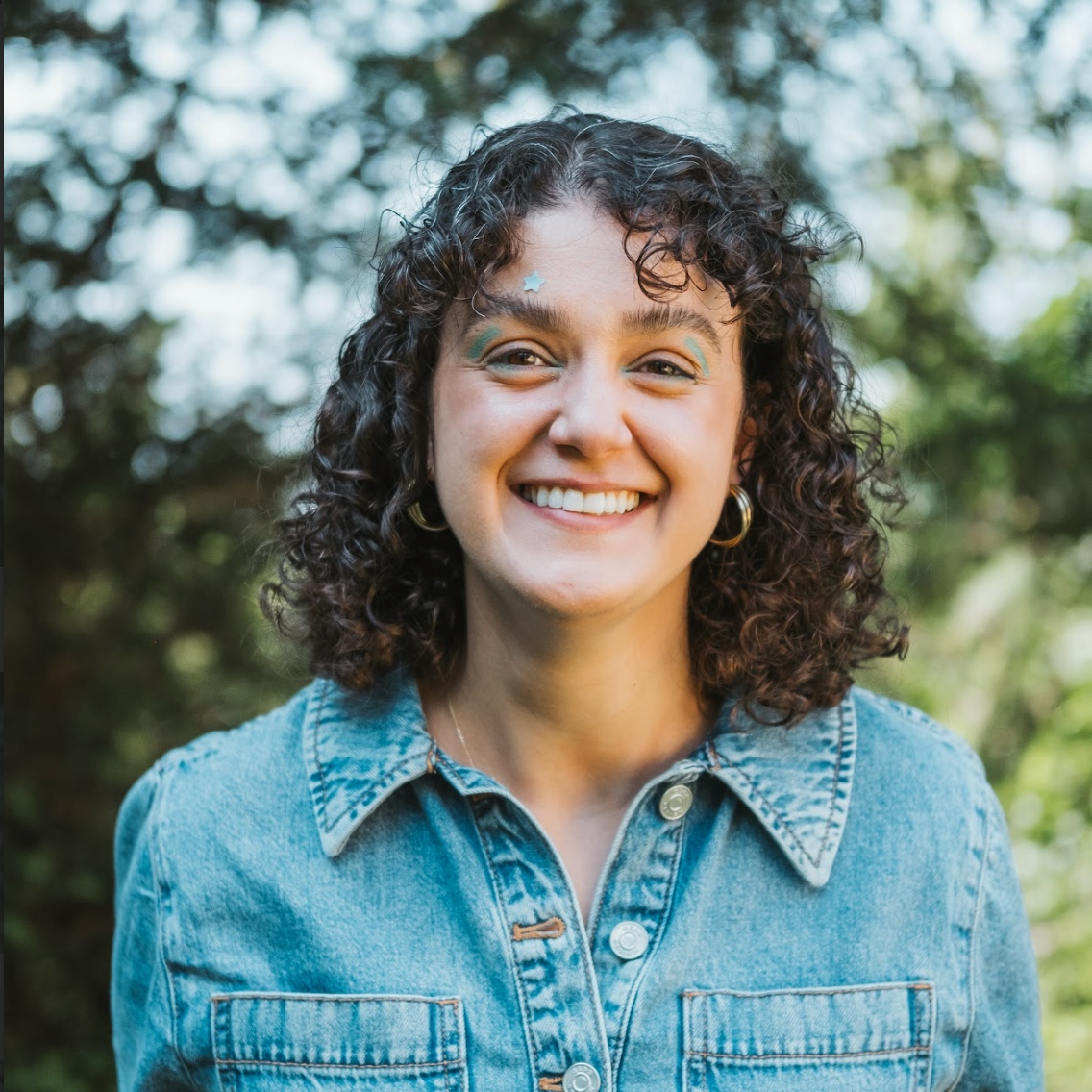 nay gulsan, a woman with dark shoulder length curly hair is smiling against a background of trees