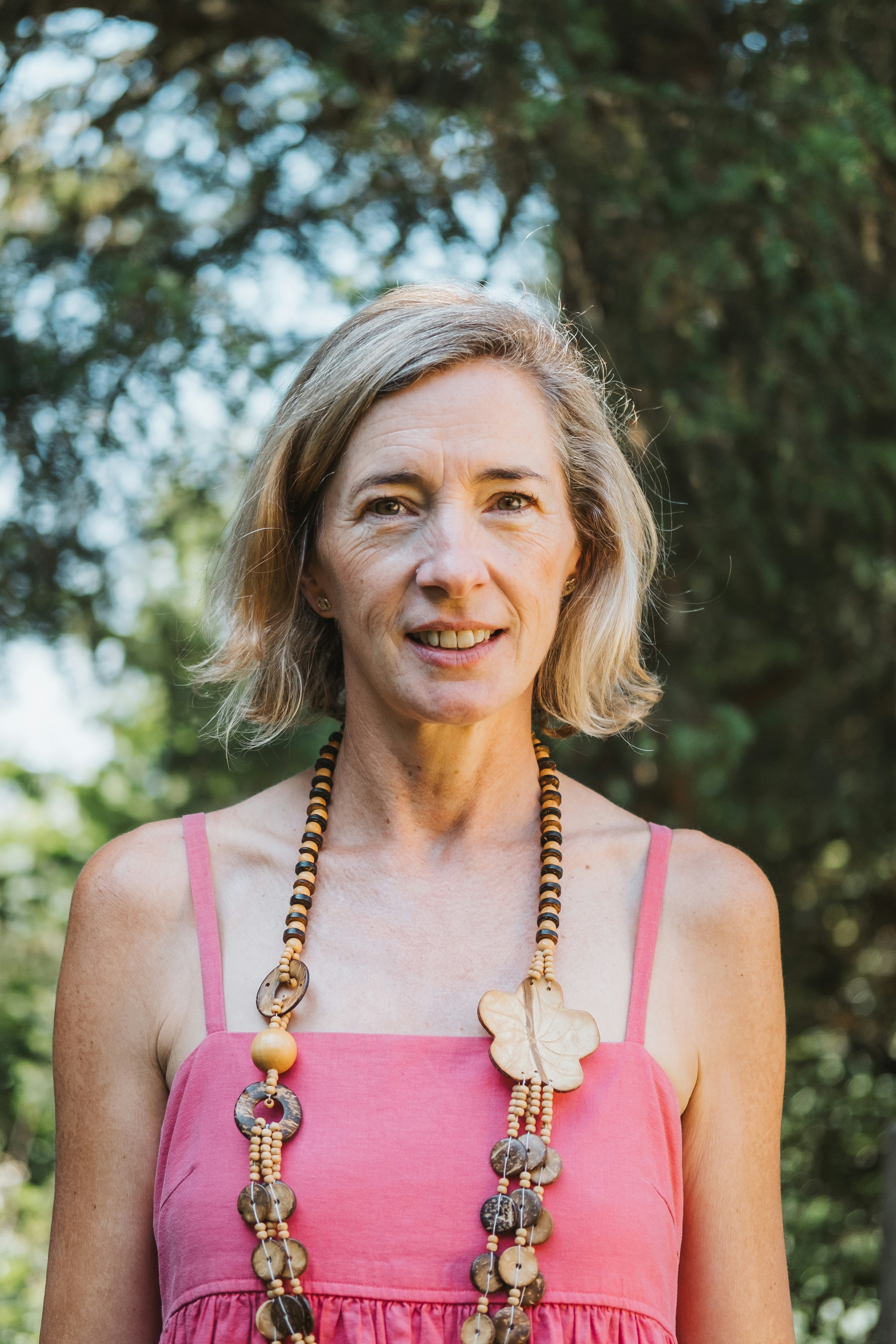 hilary strong, a woman with a short blonde bob is smiling at the camera against a background of trees