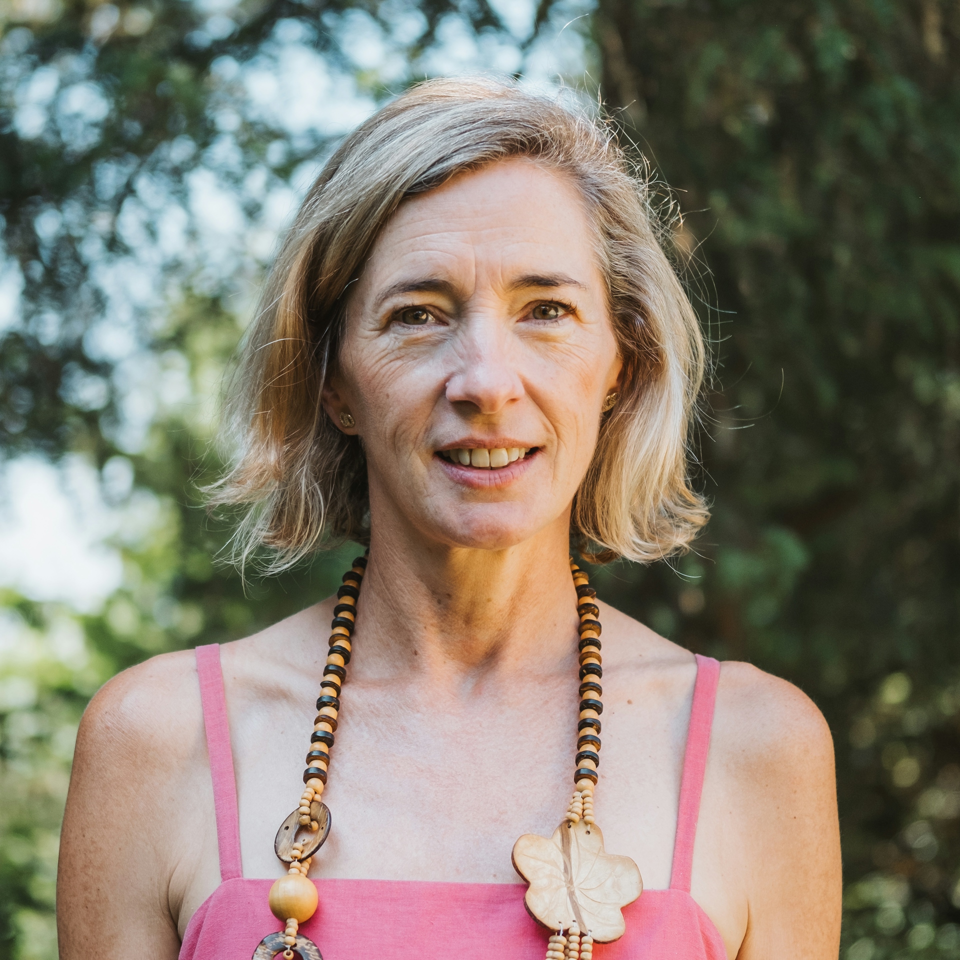hilary strong, a woman with a short blonde bob is smiling at the camera against a background of trees