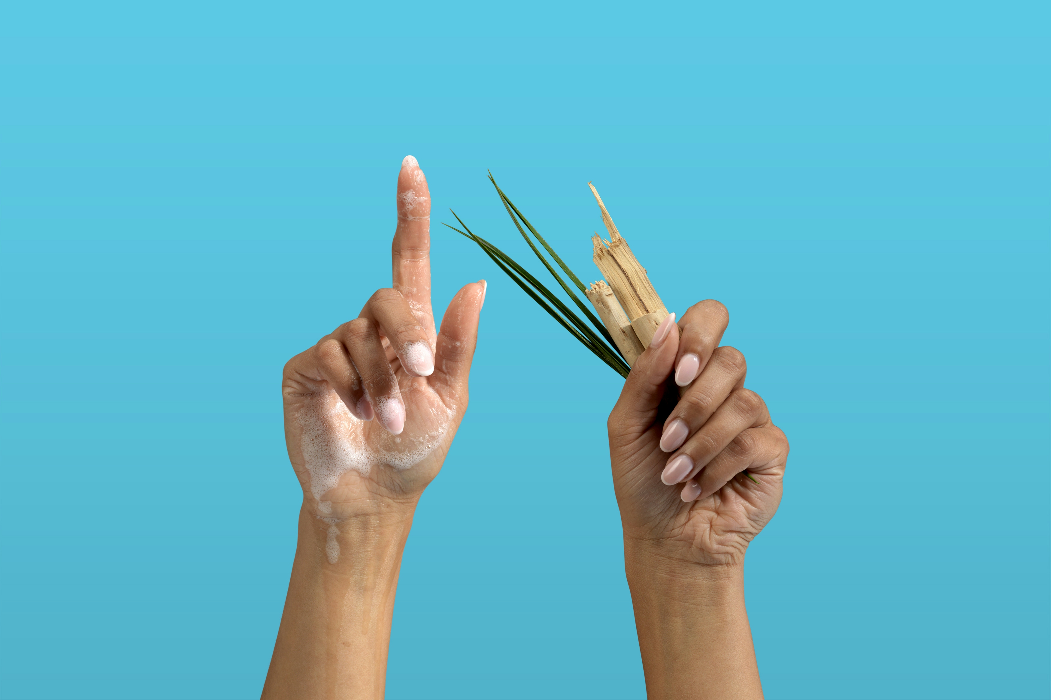 Set of hands up in the air, one hand covered in foam the other holding driftwood and seagrass