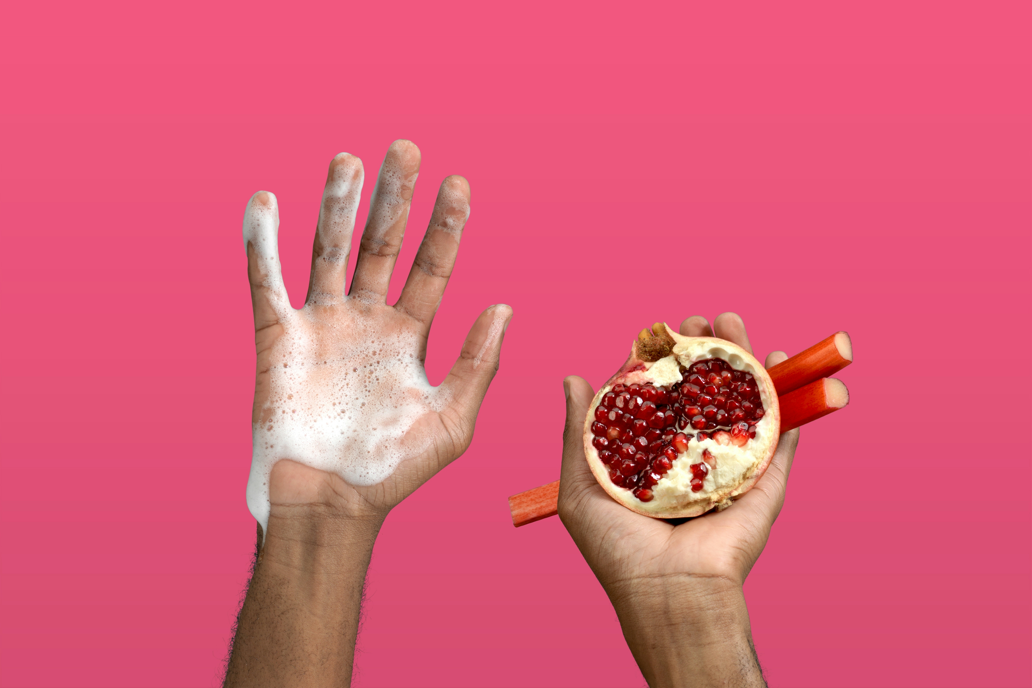 Set of hands up in the air, one hand covered in foam the other holding half a pomegranate and rhubarb sticks