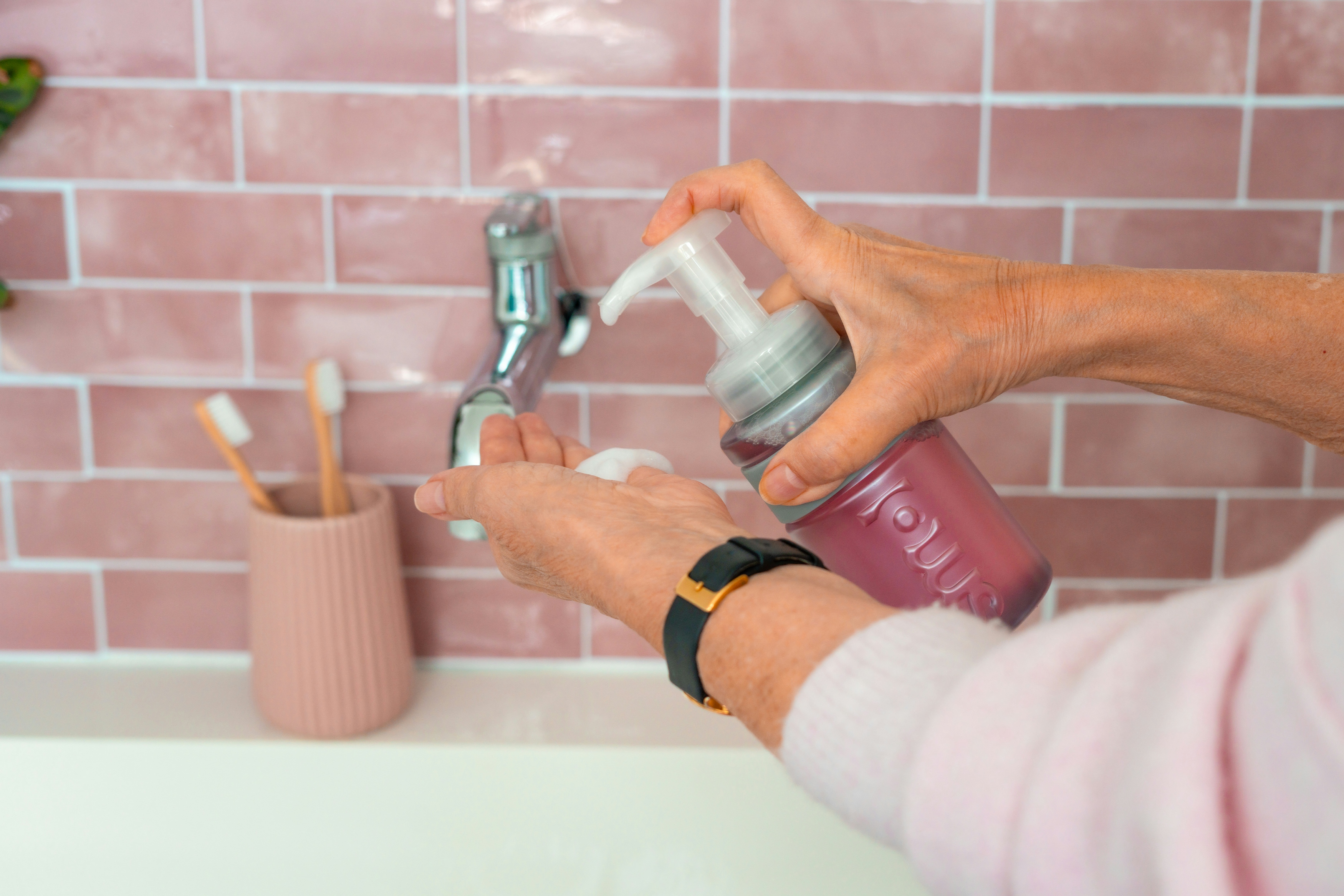 Close up of a person applying smol foaming handwash to their hand over a bathroom sink