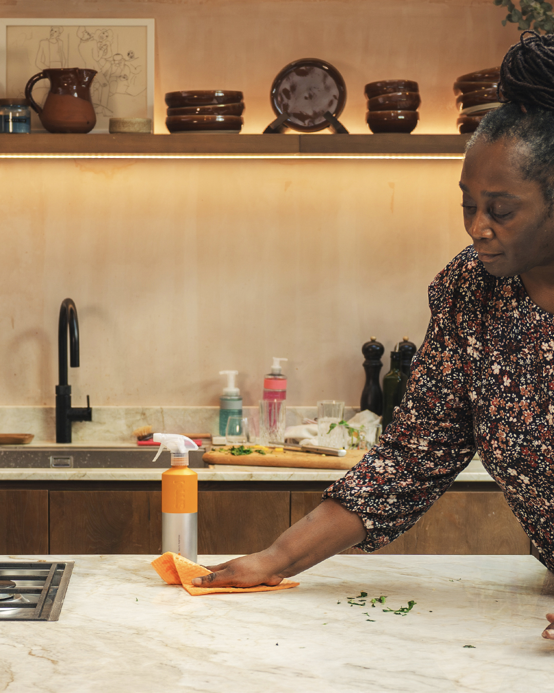 a woman wiping a kitchen counter with smol multi purpose spray and smol cloth