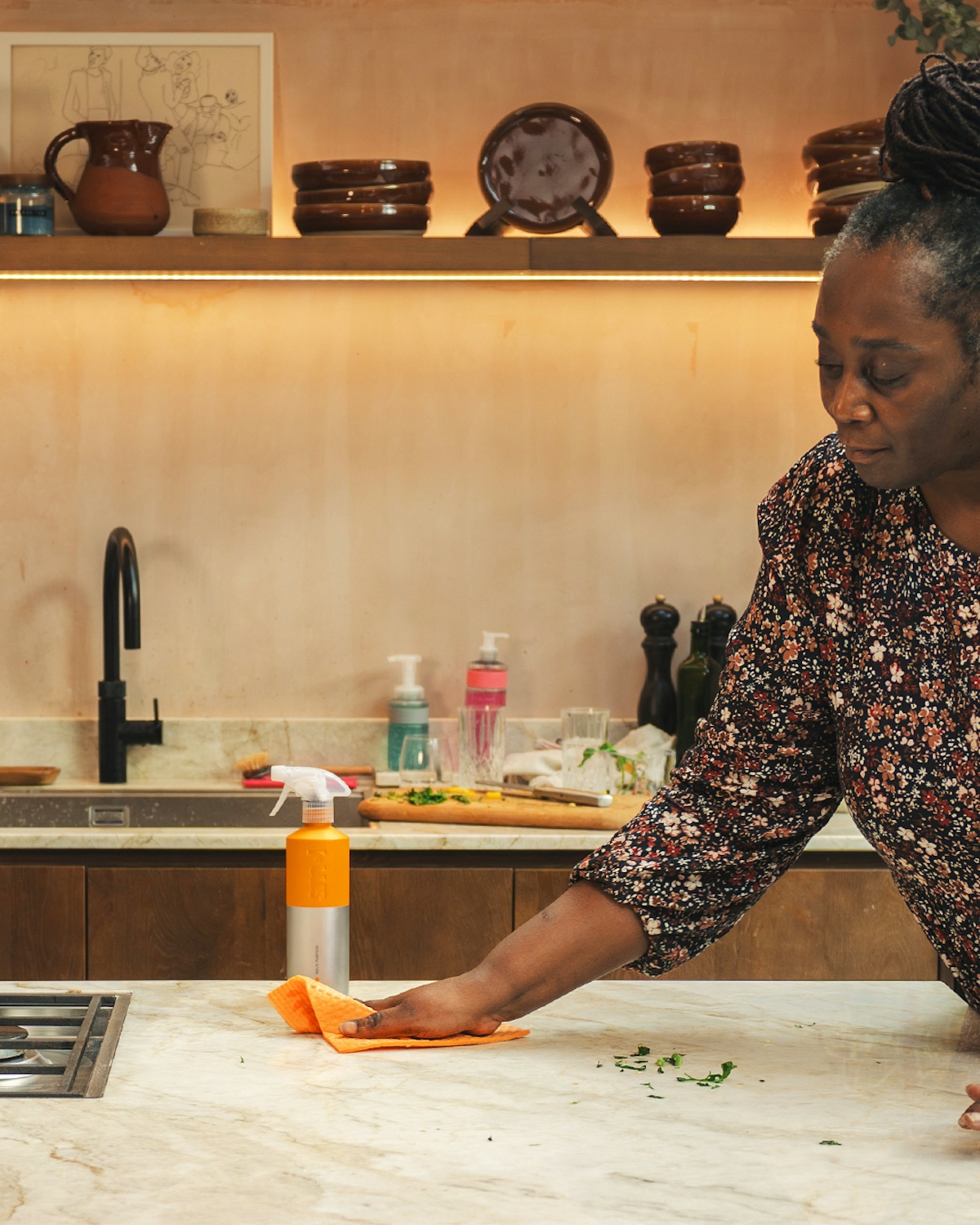 a woman wiping a kitchen counter with smol multi purpose spray and smol cloth