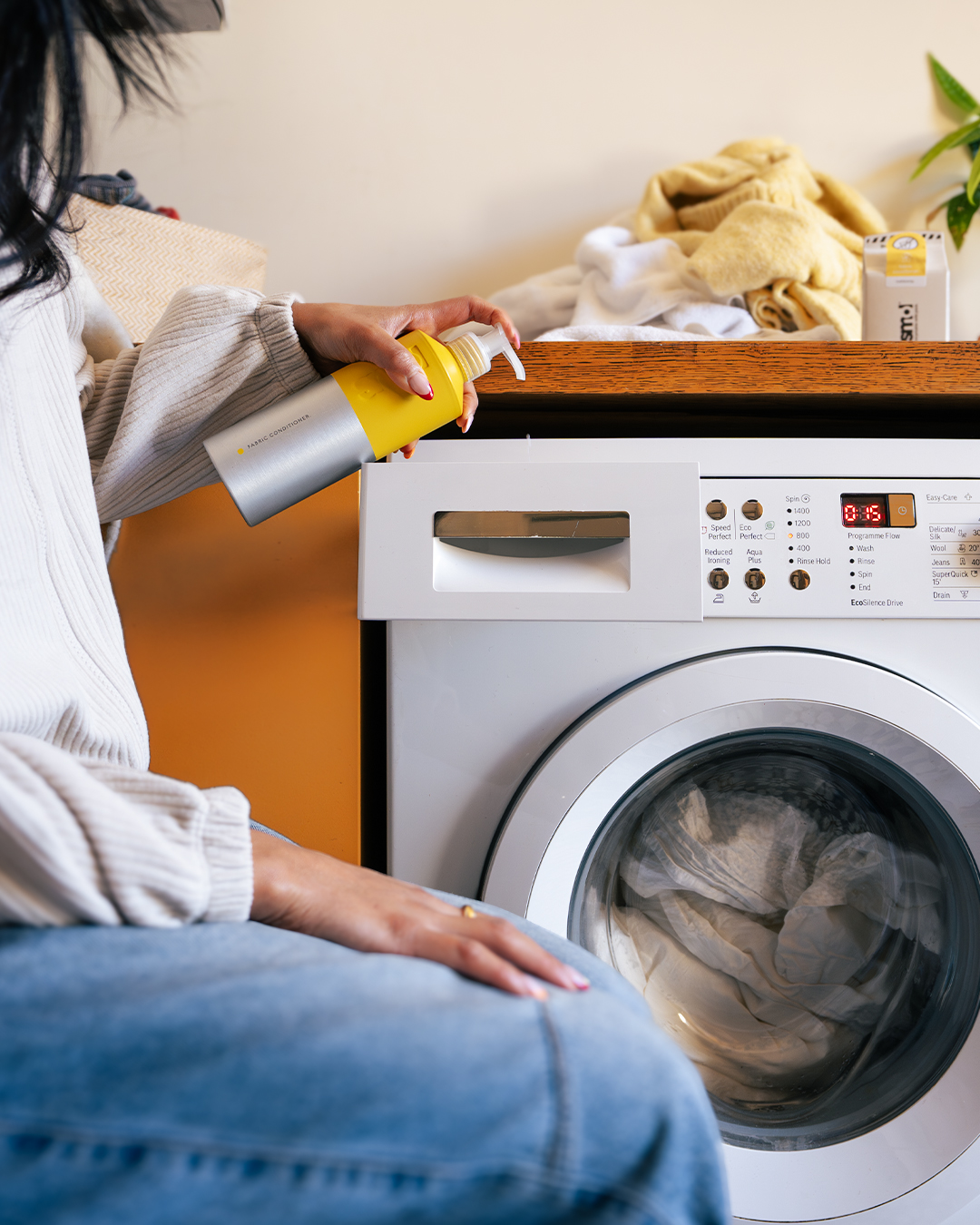 a woman sitting by a washing machine and pumping smol fabric conditioner into the drawer