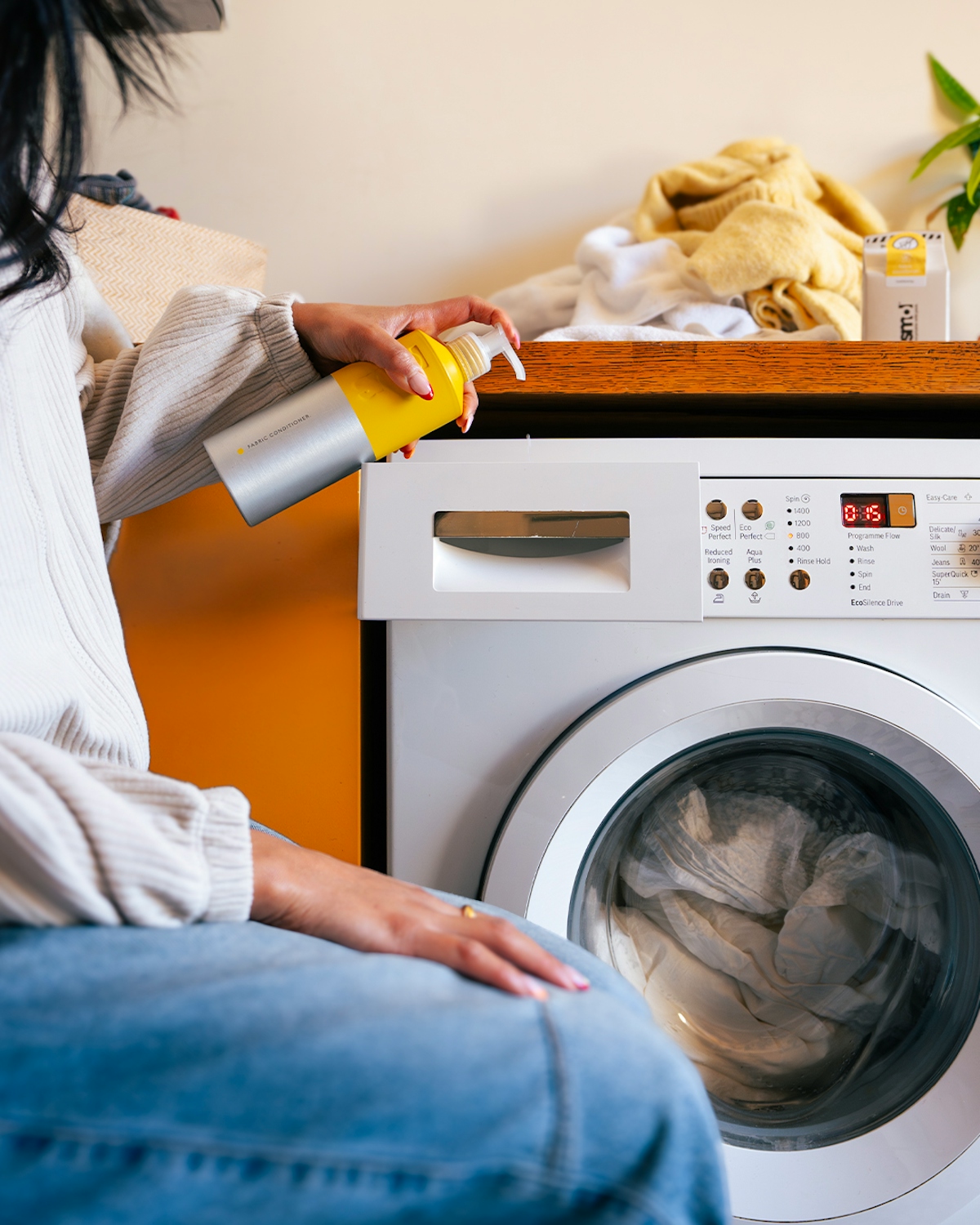 a woman sitting by a washing machine and pumping smol fabric conditioner into the drawer