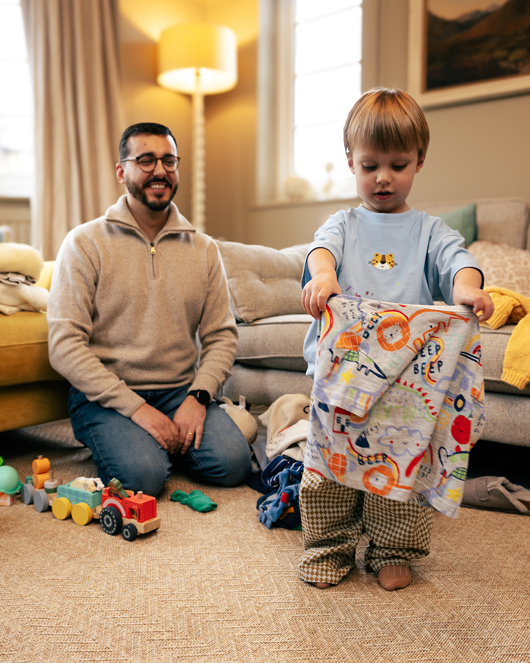a man and his child sitting in their living room with some laundry