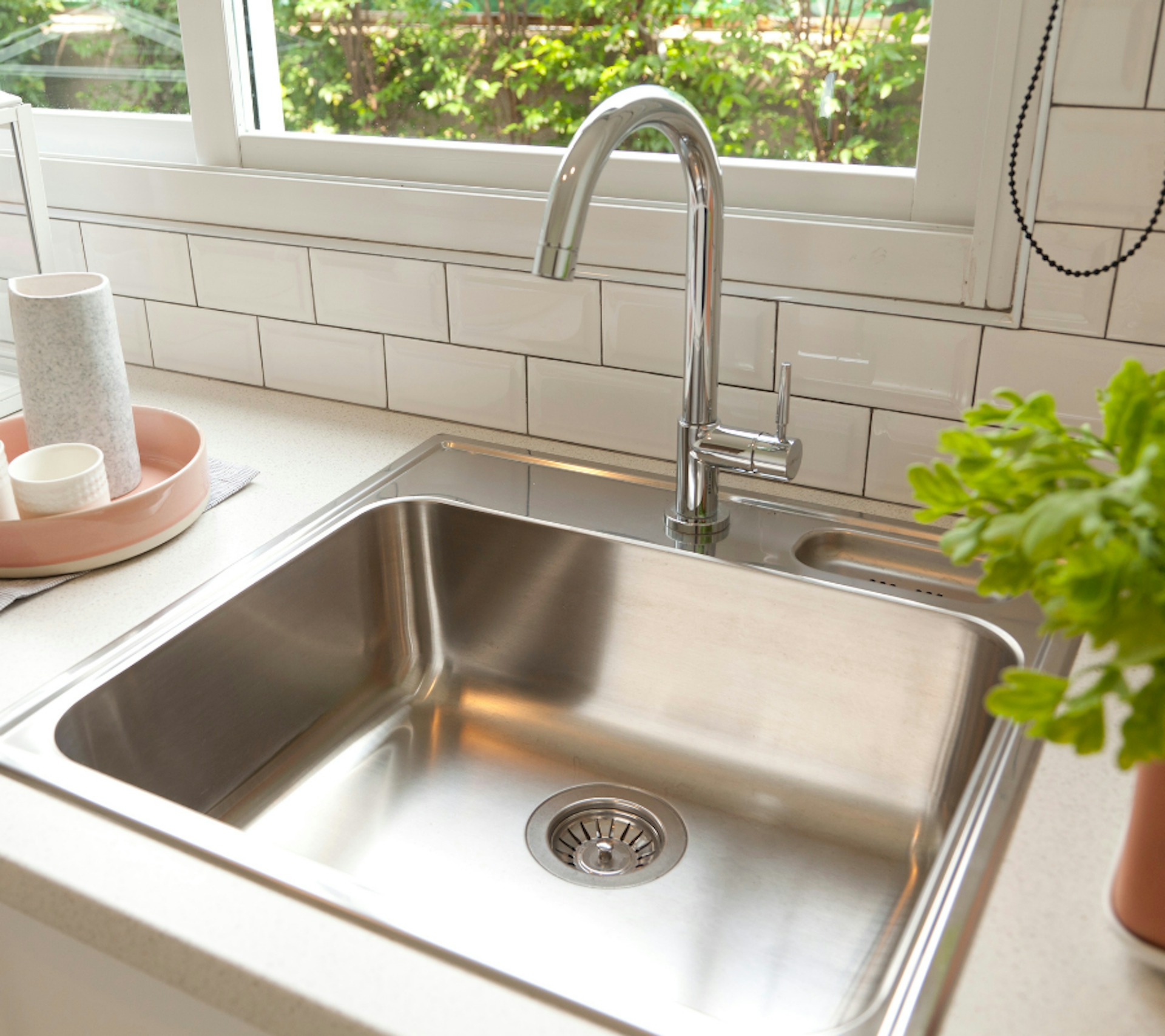 stainless steel sink with plant and white tiles