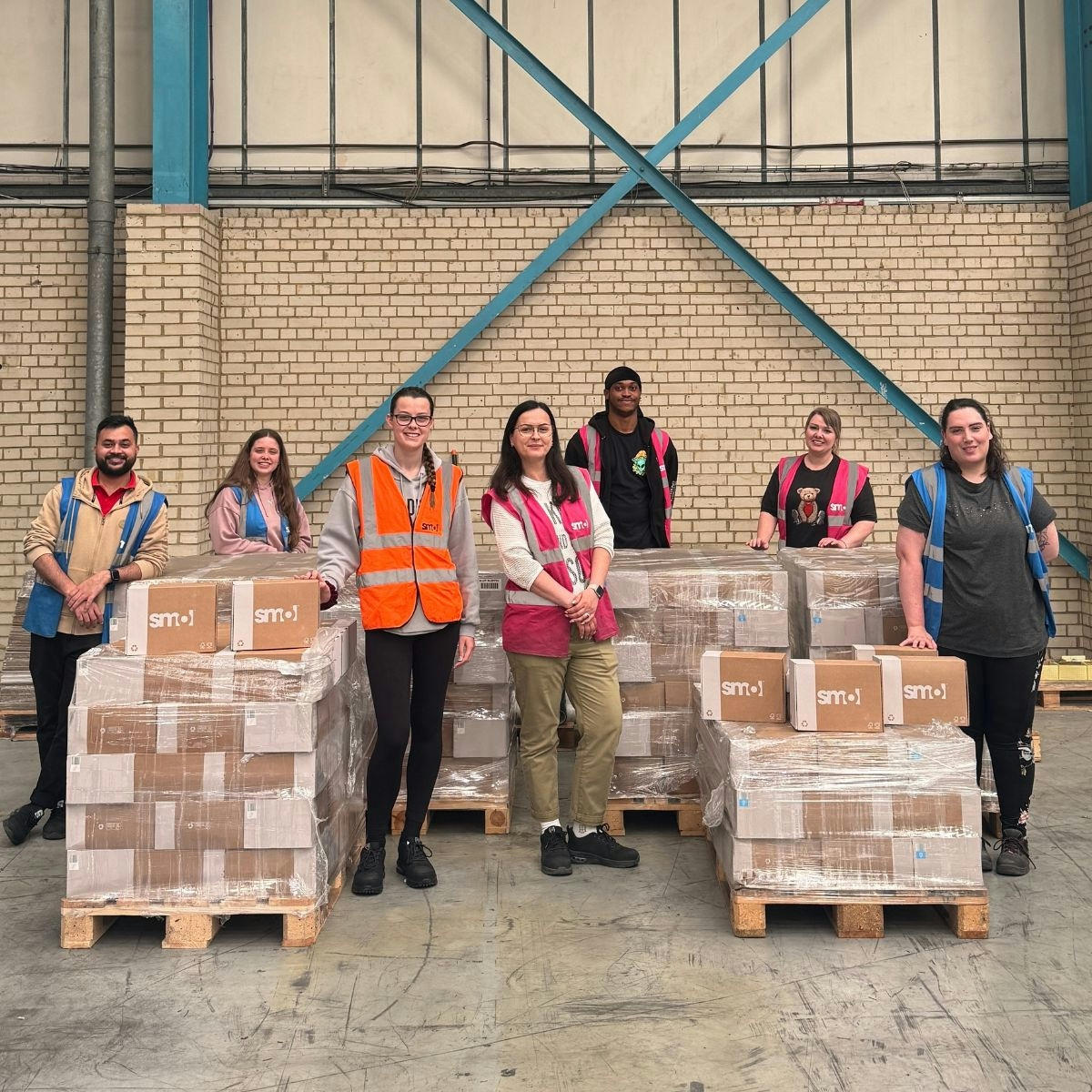 7 members of smol team stand with pallets of donation boxes for the hygiene bank