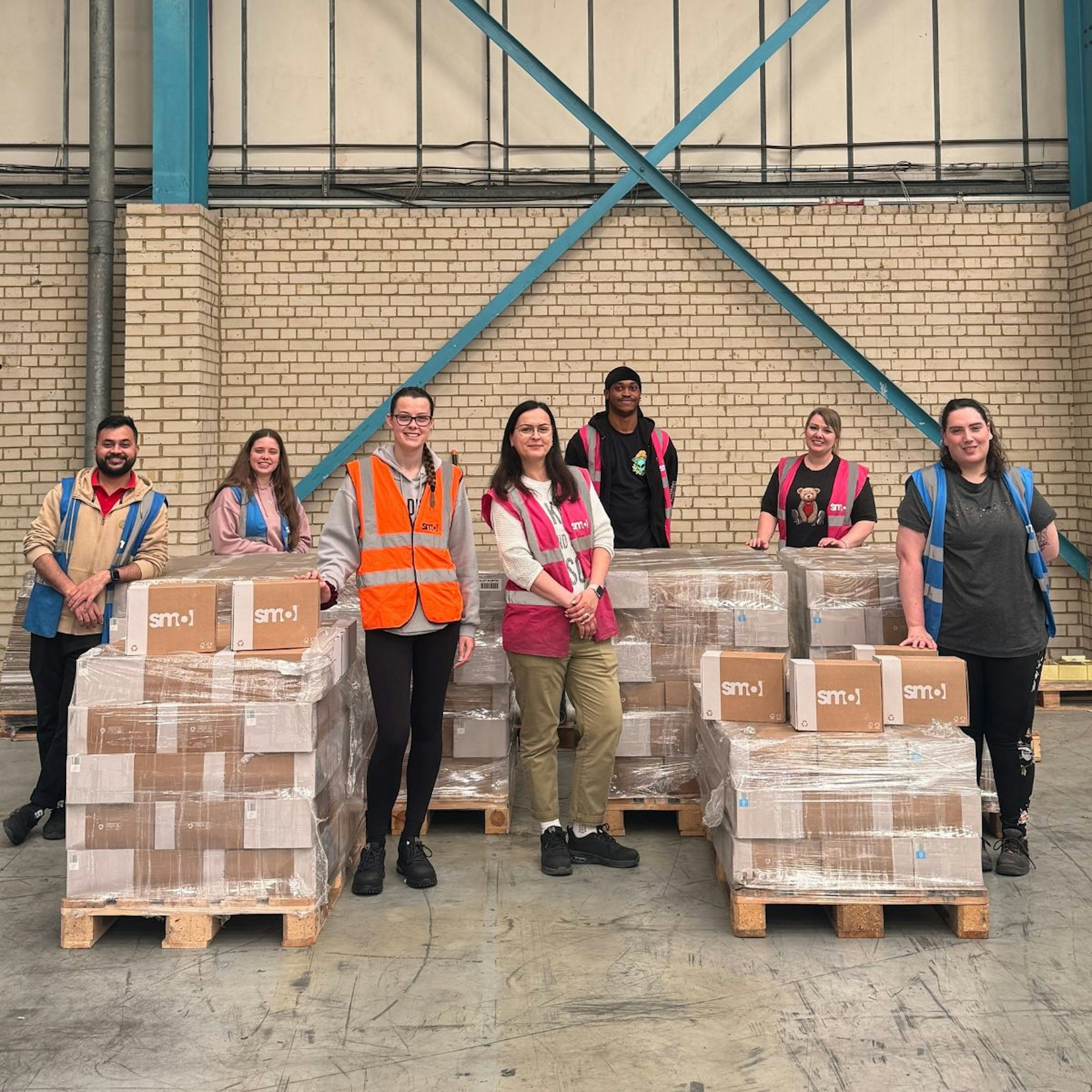 7 members of smol team stand with pallets of donation boxes for the hygiene bank